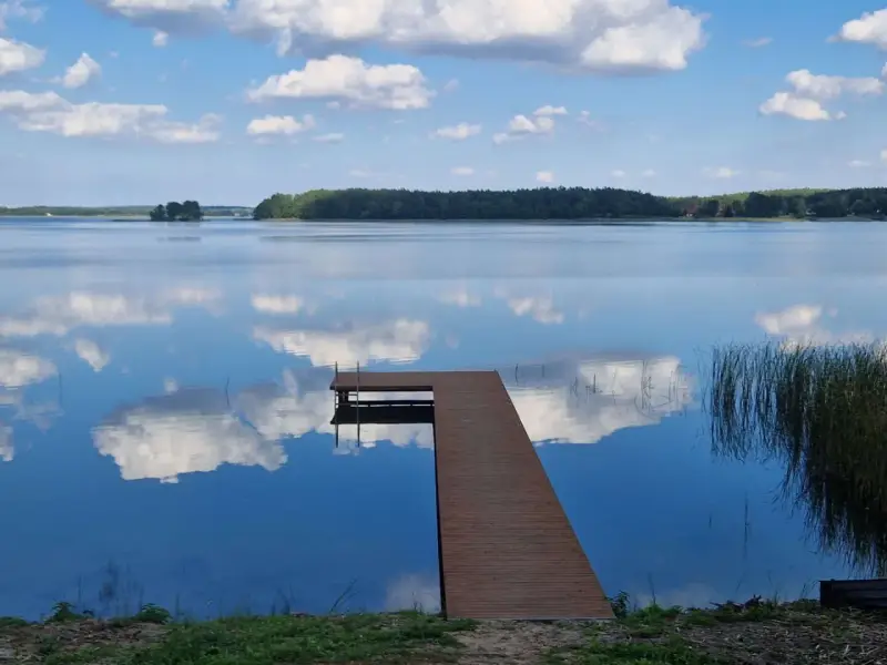 Idealne miejsce, gdzie na ryby z noclegiem Wielkopolska. Spokojne jezioro, drewniany pomost i odbijające się chmury.